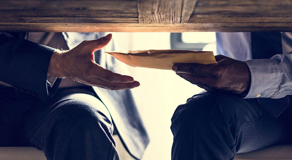 Two people discretely exchanging an envelope under a table, suggesting secrecy or a covert transaction.