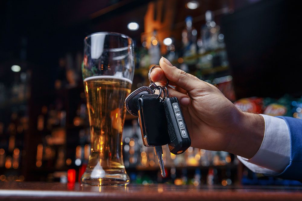 Hand holding car keys near a glass of beer on a bar counter, highlighting responsible drinking and driving awareness.