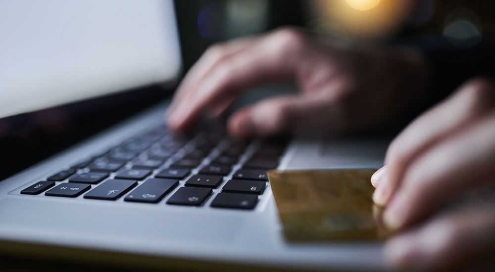 Hands typing on a laptop keyboard with a credit card, depicting online shopping or secure payment.