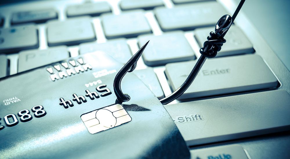 Credit card caught on fishing hook represents online phishing threat on a computer keyboard.