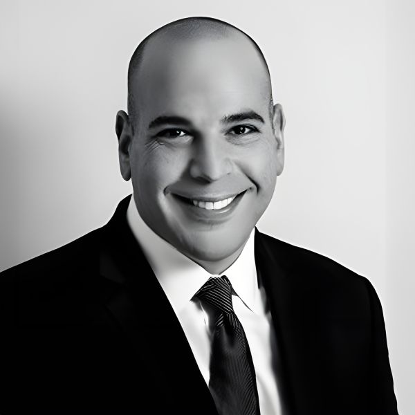 Portrait of a smiling man in a suit and tie, posing against a plain background.