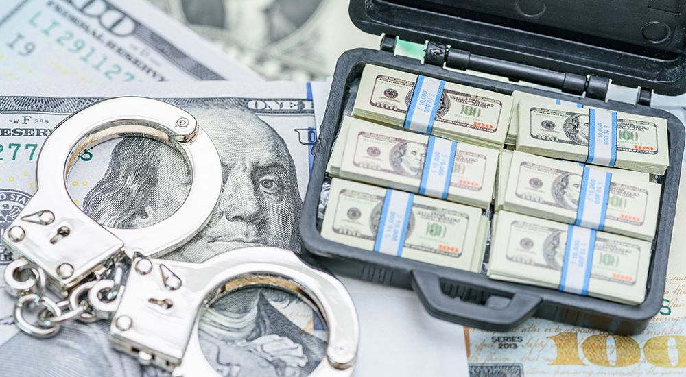 Stacks of hundred-dollar bills in a briefcase next to handcuffs, symbolizing financial crime or money laundering.