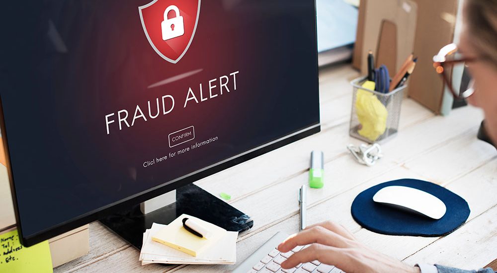 Fraud alert on computer screen with person typing at desk, focusing on cybersecurity warning.