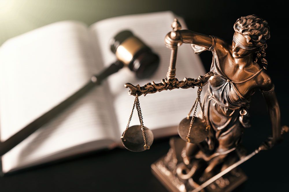 Statue of Lady Justice with scales, gavel, and open law book symbolizing fairness and legal authority.