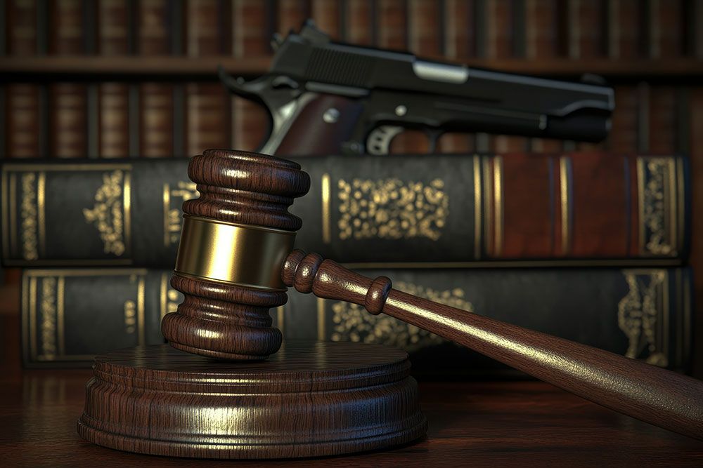 Gavel and law books with a handgun in the background, symbolizing legal issues related to firearms.
