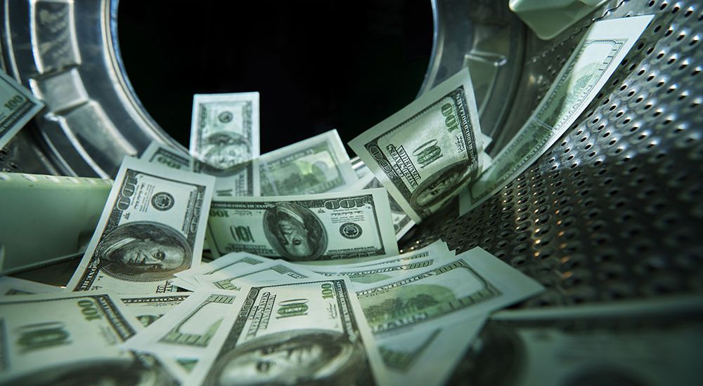 Hundred-dollar bills inside a metal washing machine, representing money laundering concept.
