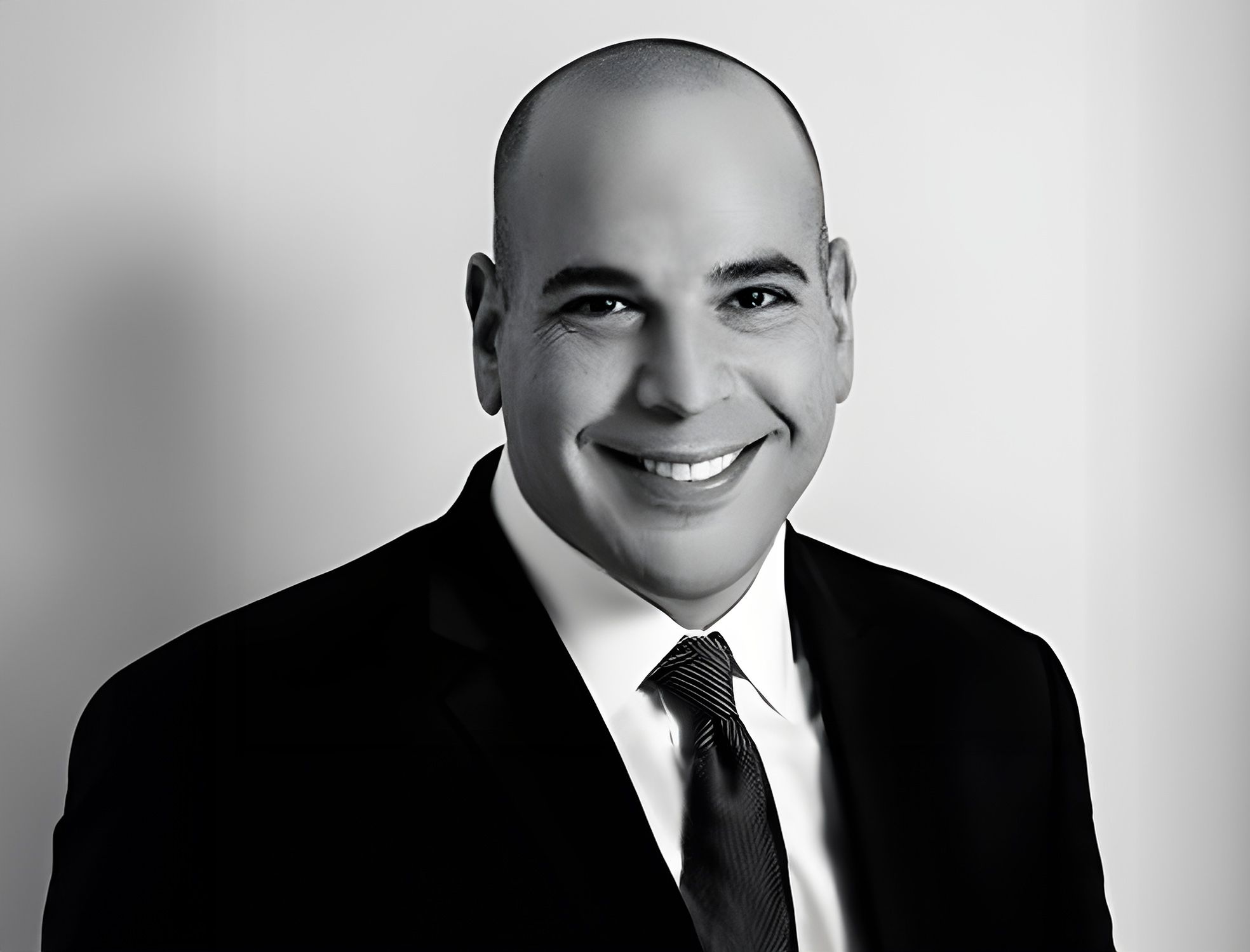 Smiling man in a suit and tie poses in a professional black-and-white portrait.