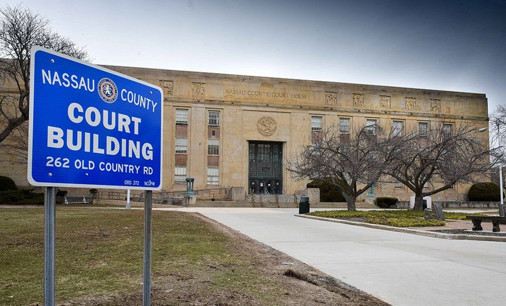 Nassau County Court Building entrance with sign at 262 Old Country Rd, surrounded by trees.