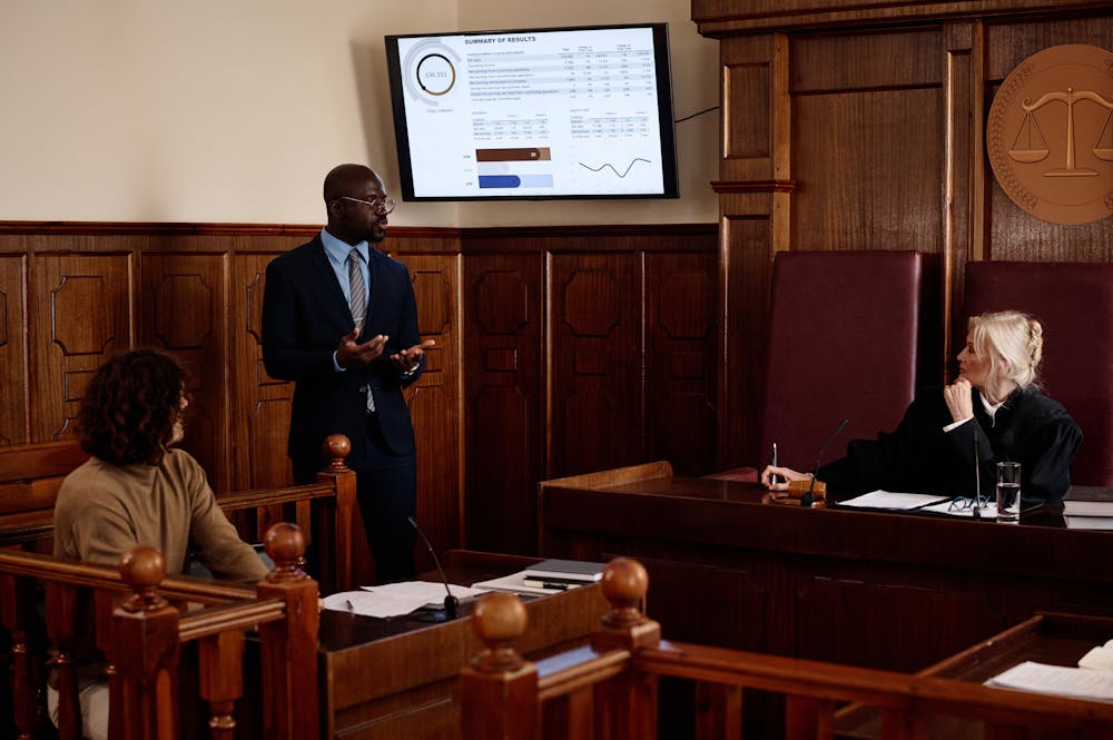 Man presenting data in courtroom with judge and audience.