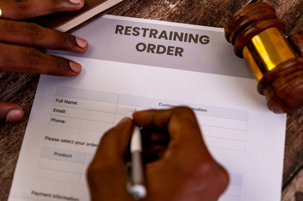 Person signing a restraining order document with a gavel on a wooden table.